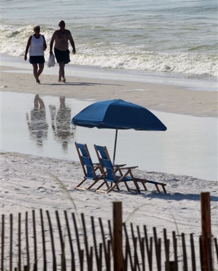 People walk past empty beach chairs in Destin, Fla., on Sunday. Some hotels and condominium owners along the Gulf say their business is down by 50 percent. 